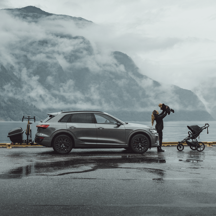 A car is parked by the water next to a family with a Thule Santu towbar cargo carrier